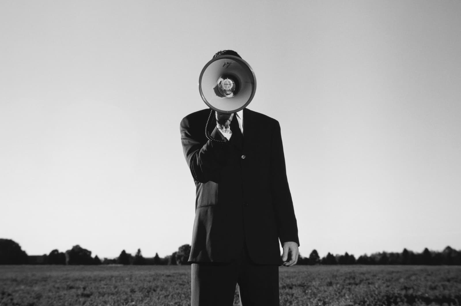 A person standing in a field wearing a suit with a megaphone covering their face