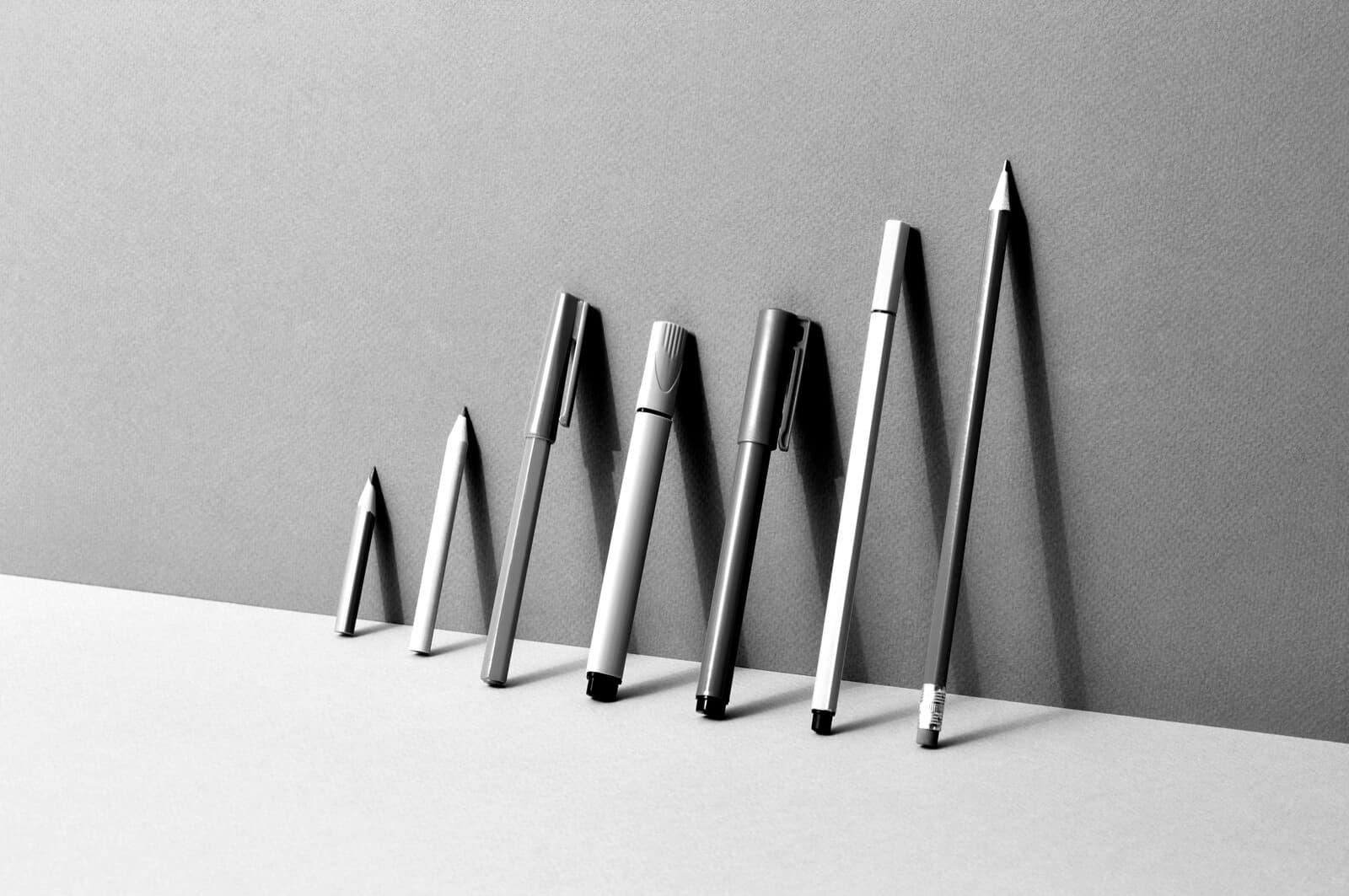 A row of pens and pencils leaning against a wall