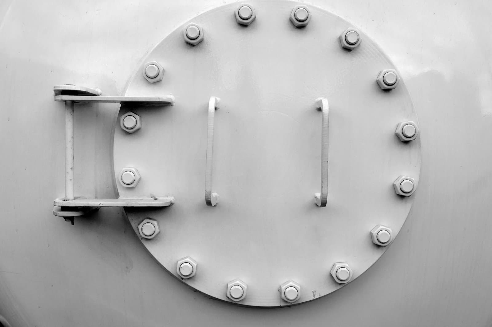 A grey image of a heavy metallic round door with large secure screws and bolts for safety