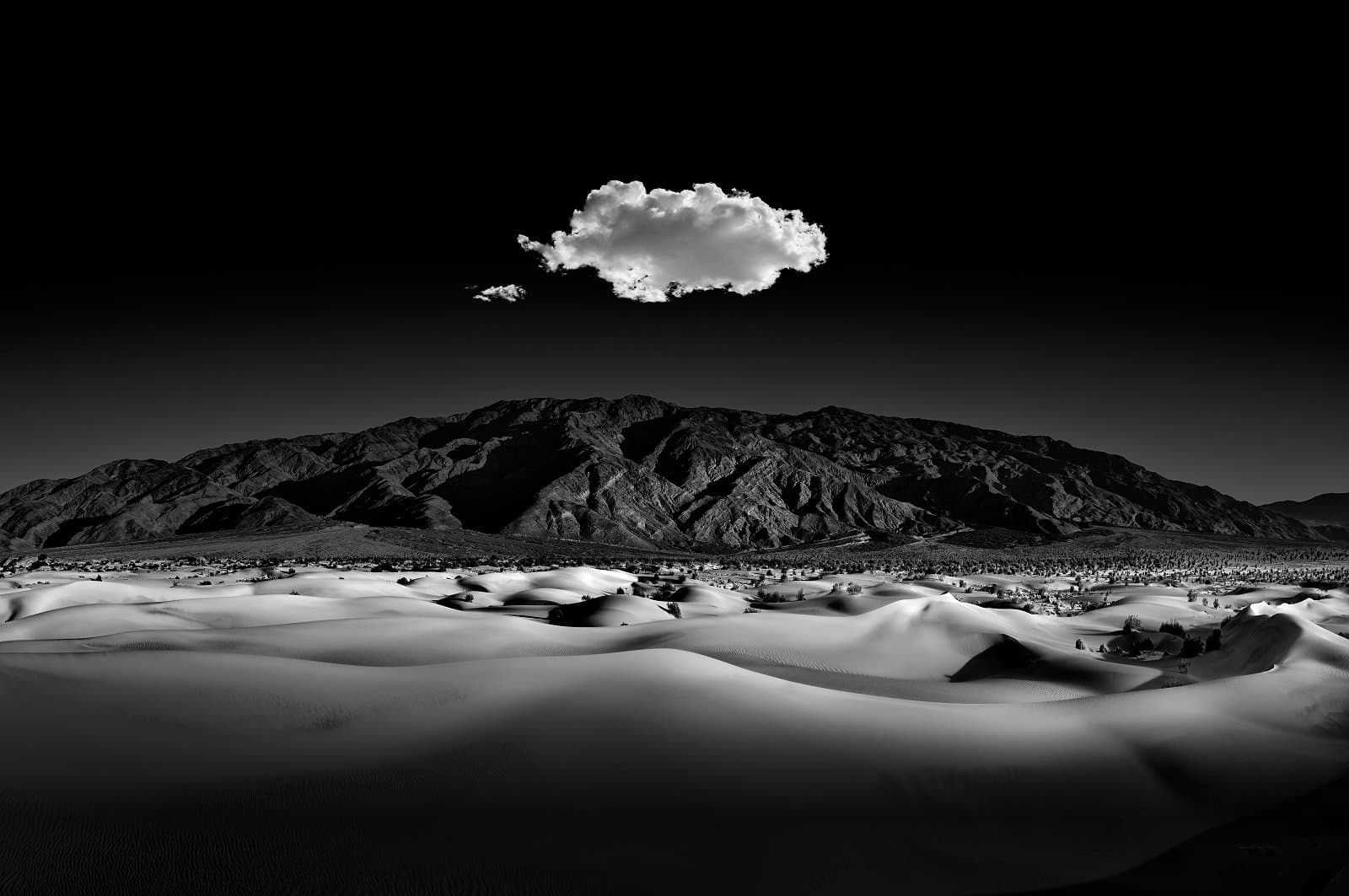 Mesquite dunes of death valley with the Amargosa Mountains in the distance. Curves, patterns, and shadows captured and contrasted in the moonlight. A single cloud hangs above, serenading the evening landscape.