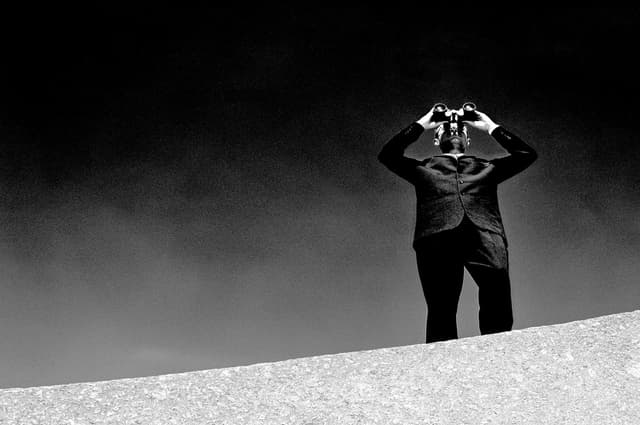 Man in suit looks through binoculars