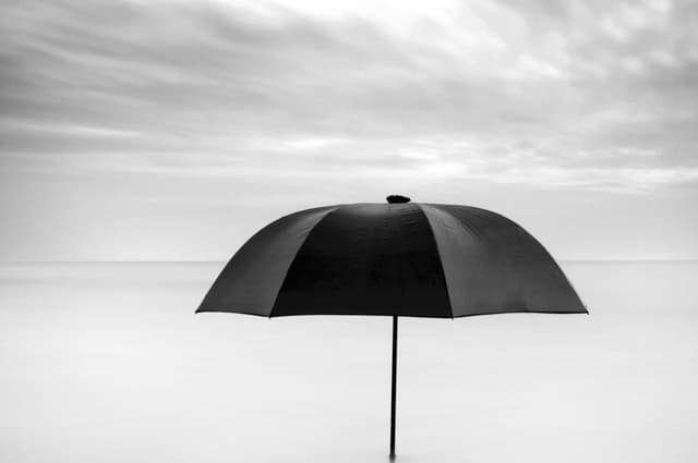 A black umbrella in the middle of a desert, standing in the sand