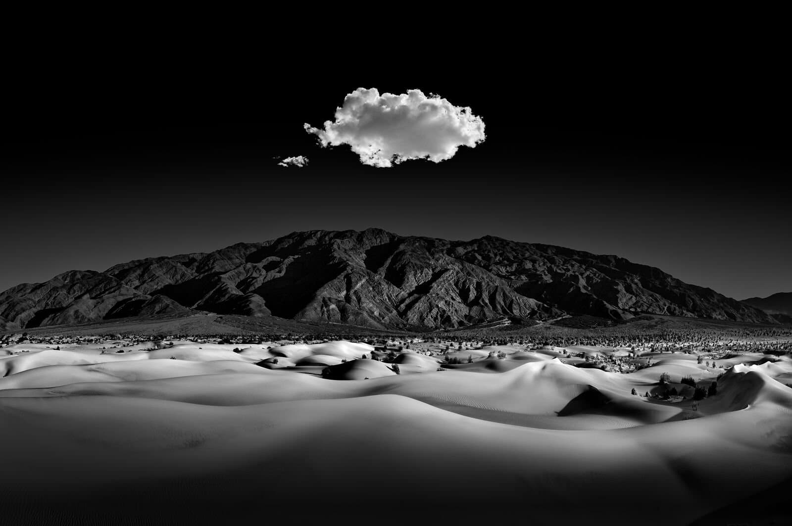 A cloud hovering over a desert with mountains in the distance