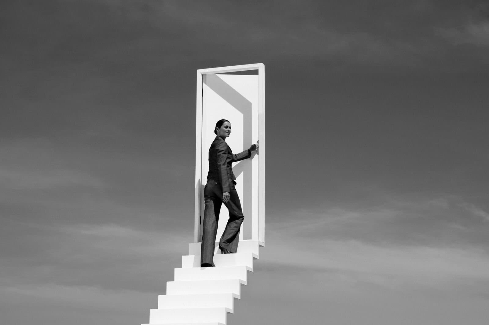 A person walking up a set of stairs leading to a door in the clouds